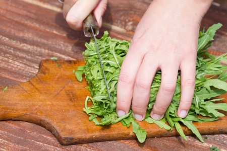 Woman makes fresh salad on a wooden table . greens , summer , natureの写真素材