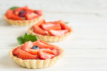 Mini tartlets with fresh strawberries and custard on a wooden tableの写真素材