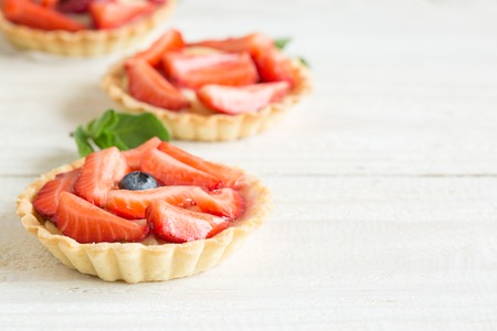 Mini tartlets with fresh strawberries and custard on a wooden tableの写真素材