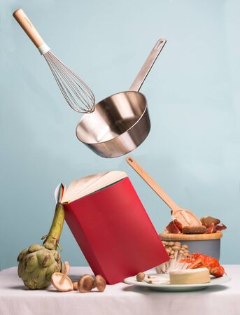 Concept of flying food preparation with seafood, artichoke, mushrooms and cheese using recipes book and stewpan with whisk. Art pictureの写真素材