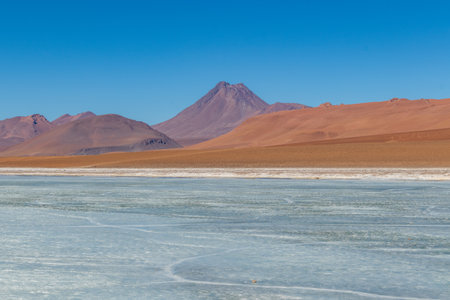 Landscape with frozen lagoon and volcano in the background, in the Atacama Desert.