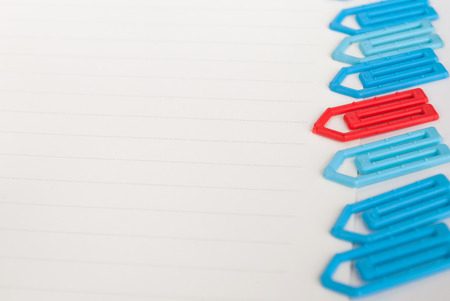 many blue and one red paper clip on a white paper with space for textの写真素材