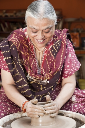 senior potter shaping up the terracotta clay pot on wheal の写真素材