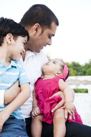 little baby girl and a little boy sitting in the lap of the fatherの写真素材
