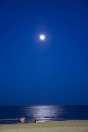 A night shot of two blurry people in the beach illuminated by the moonの写真素材
