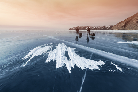 Baikal in winter, two travelers go on the ice at sunset. Russia, Siberia.の写真素材