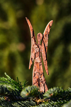 A Christmas angel made of wood isolated behind a pine branch and in front of a natural green backgroundの写真素材