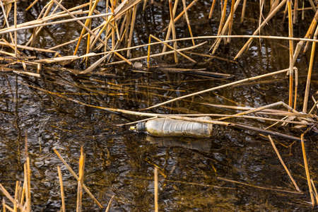 A plastic drinking bottle was thrown away and is slowly rotting in a body of waterの写真素材