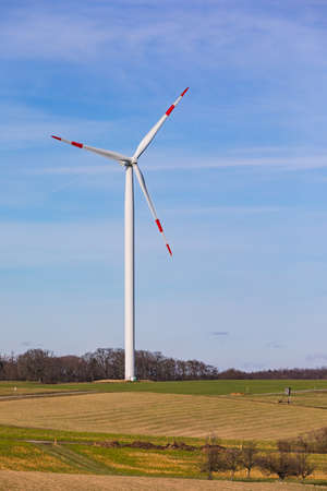 A modern wind turbine with white propellers on a hill