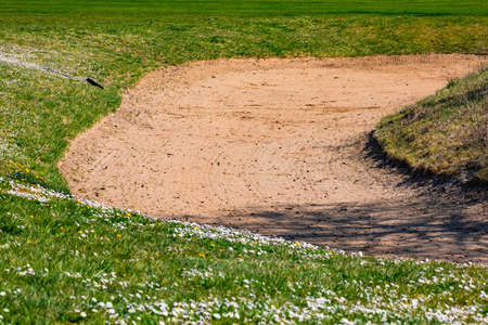A sand bunker with rakes on a golf course in Germany with sand and lawn lined with daisies in Springの写真素材