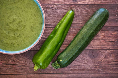Fresh vegetable detox soup made from peas in a plate on brown wooden table with cucumbers and green pepper, top view with space for text. Tastyの写真素材