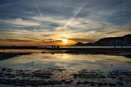 sunset with reflections and beautiful clouds with many colors, on the Albufereta beach in Alicante,...