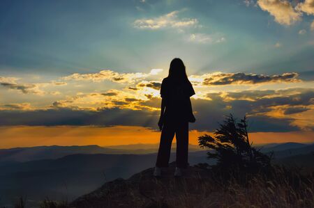 Silhouette of a young girl on a background of beautiful sunset in the mountainsの写真素材