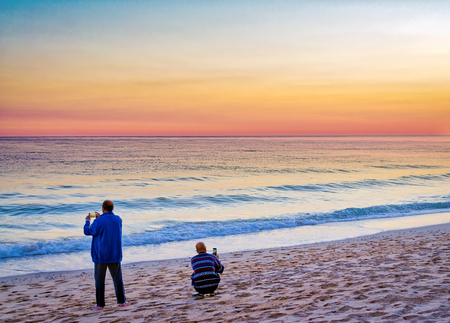 Back view of two people shooting the majestic sky on the beachの写真素材