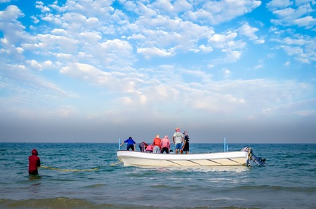 Group of fishermen trying to drag the net full of fish to the boat, while one holding the rope to...