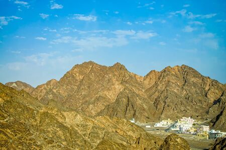 A small town surrounded by large pointy mountains on a clear sunny day. From Muscat, Oman.の写真素材