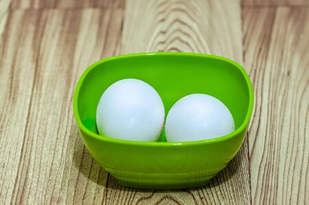 Two eggs in a green bowl on a wooden tableの写真素材