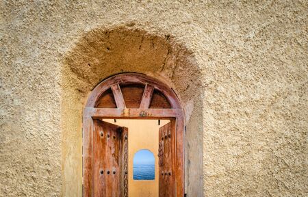 Old, antique door of a watchtower opening to reveal a arch window to the sea. From Muscat, Oman.の写真素材