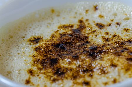 Closeup of froth in a coffee cup with coffee powder on top