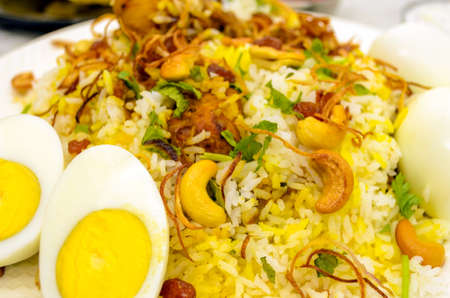 Closeup of chicken biryani plate with cut eggs in the foreground with fried onions and cashew nuts spread onの写真素材