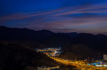 Illuminated small town surrounded by mountains and the road leading to it. From Muscat, Oman. Long...