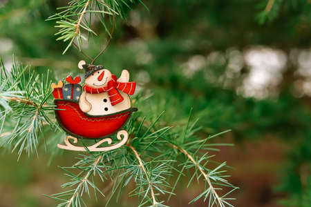 A wooden toy in the form of a snowman in a sleigh with gifts hangs on the Christmas tree. Copyspace....