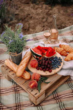 A summer picnic in nature. Fruits, baguettes, croissants and wine stand on a wooden table. Beautiful rustic decor.の写真素材