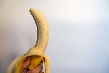 One ripe banana, peeled, held in hand, with a white back.の写真素材
