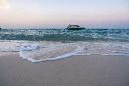The boat floats on the seashore, seeing the small waves, hitting the sand.