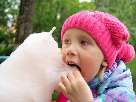Little girl eats a cotton candy in the parkの写真素材