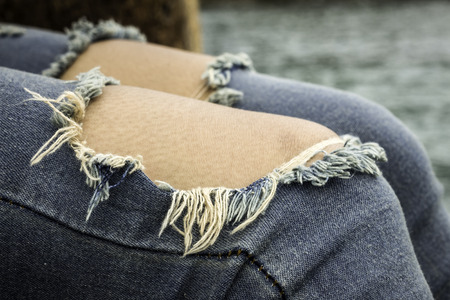 Jeans with two big holes and bits of thread in the kneeの写真素材