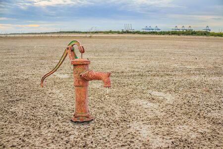 Rusty water pump on land with dry and cracked ground. Desertの写真素材