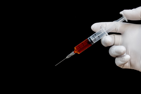 Syringe in a hand in medical gloves, ready for injection with medication. Black backgroundの写真素材