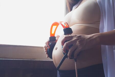 Abdomen to the baby listening to music by the window.の写真素材