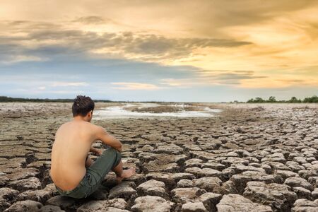 Water crisis, man sit on cracked earth near drying water.