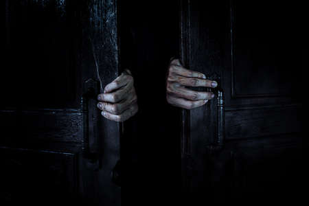 Ghost hands open the wooden door from the inside of the old dark room. Filled with spider webs