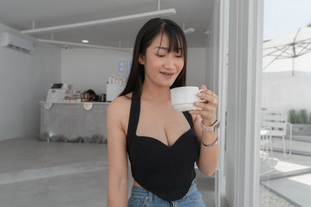 Beautiful sexy asian woman in black dress Drinking coffee in a white minimalist style coffee shop, enjoying the holidays.の写真素材