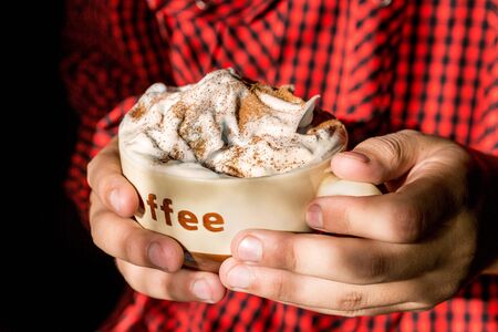 A cup of coffee with cream and cinnamon in teenager hands.の写真素材