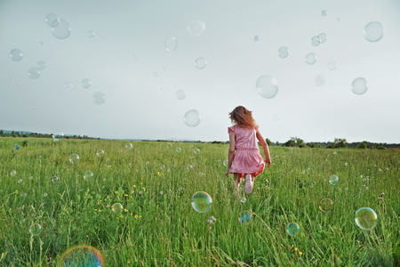 Little girl is playing among soap bubbles on green meadow in summerの写真素材