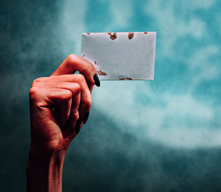 Red demon or devil hand holding empty card on dark  moon, space for text. Halloween/horror themeの写真素材