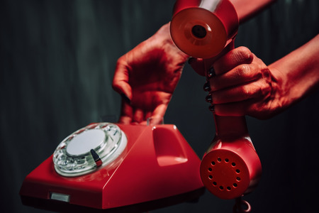 Red hands of devil giving retro phone on dark . Halloween or horror themeの写真素材