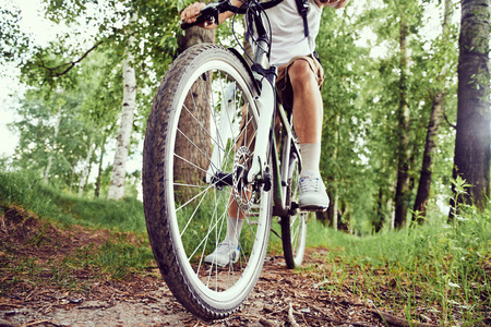 Unrecognizable man is riding bicycle on trail in summer park