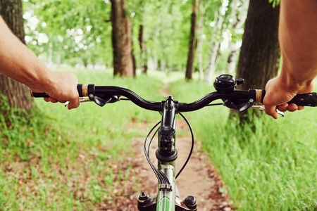 Close-up image of cyclist man hands on handlebar riding mountain bike on trail in summer park, face is not visibleの写真素材