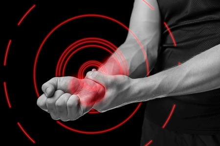 Pain in a male wrist. Man holds his hand, monochrome image, pain area of red colorの写真素材