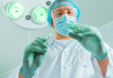 Doctor surgeon holds a scalpel in an operating room, focus on scalpelの写真素材