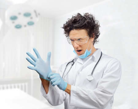 Funny man doctor is putting on gloves in a hospitalの写真素材