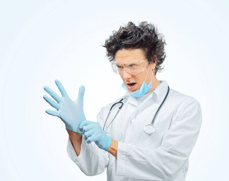 Funny man doctor is putting on gloves in blue backgroundの写真素材
