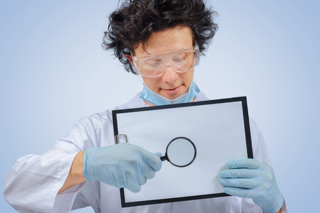 Funny man doctor holds clipboard and magnifying glassの写真素材
