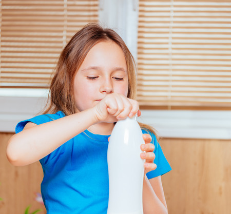 Little girl is opening bottle of milk indoorsの写真素材