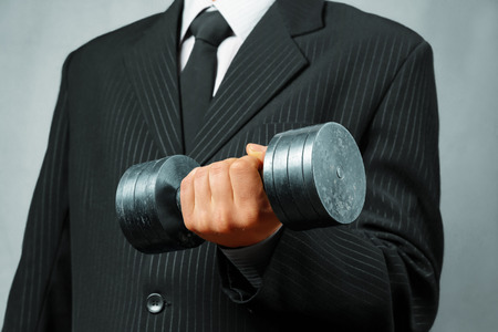 Unrecognizable strong businessman in a suit holds metal dumbbellの写真素材